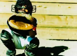 Baseball catcher in full gear crouched behind the plate, locked in and focused on the pitch.